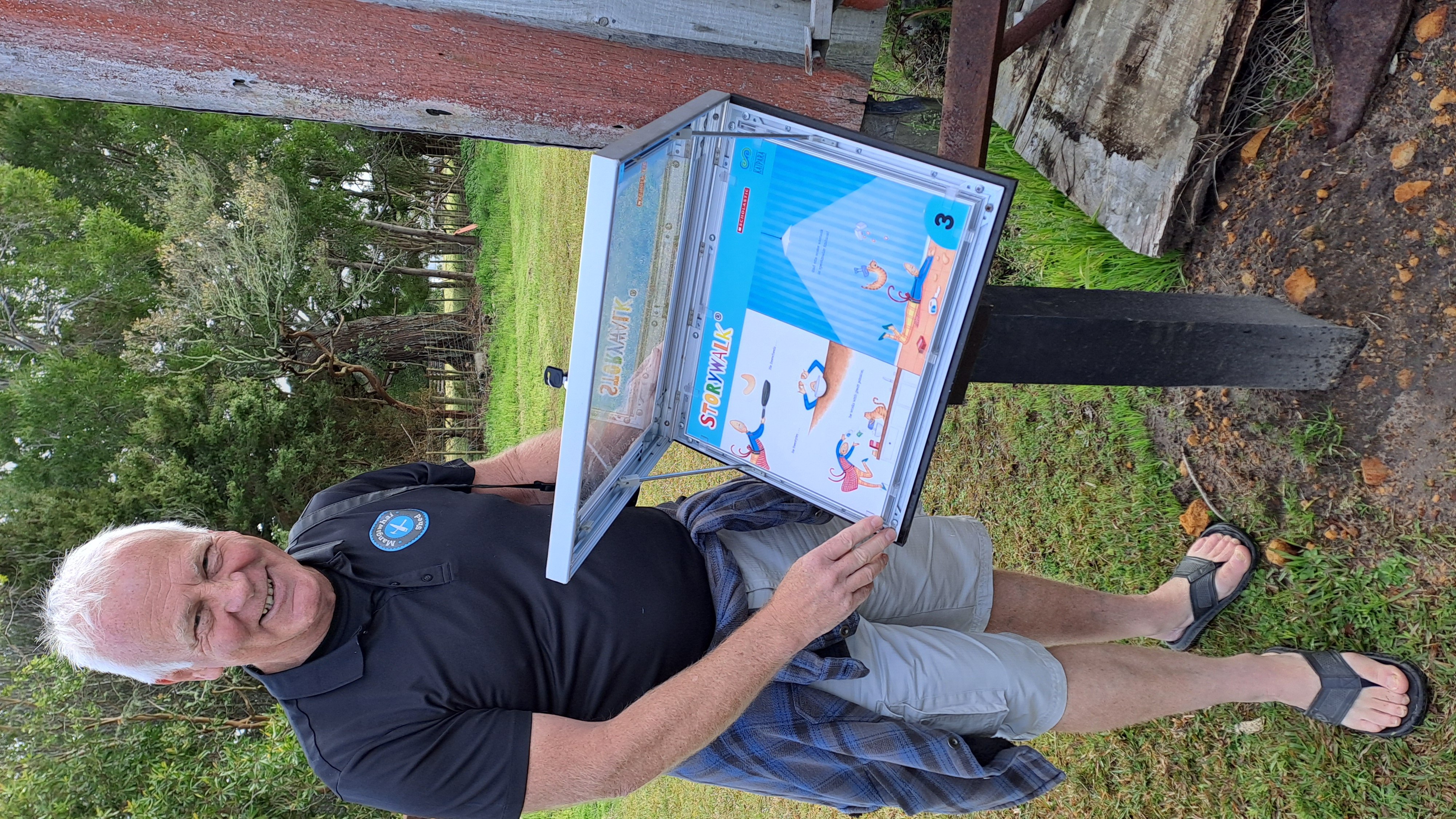 A man facing the camera and smiling next to an open demonstrates how to open Storywalk board